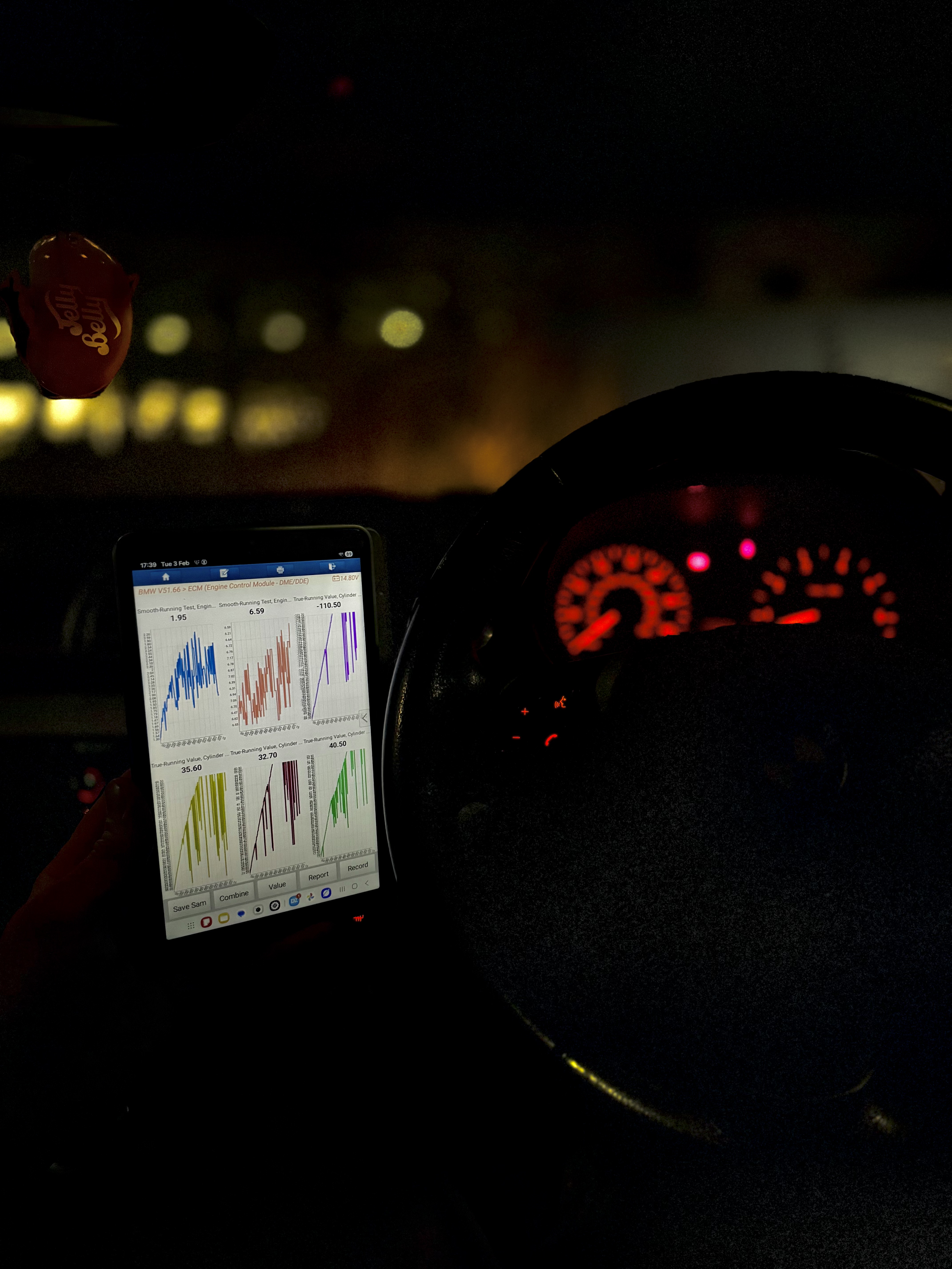 Diagnostic tablet showing engine data beside the vehicle instrument cluster